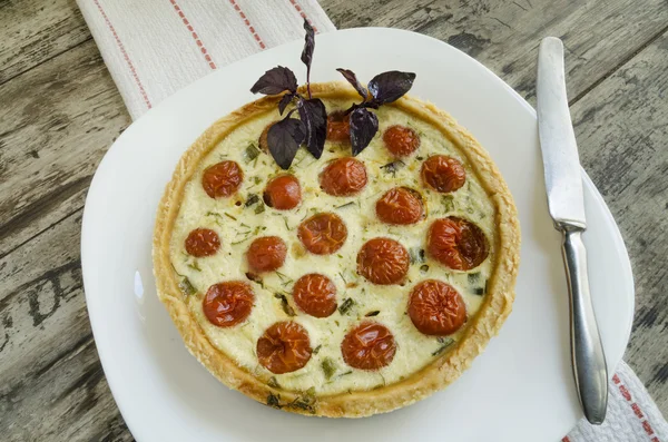 Tart com tomate cereja, queijo e cebola na placa branca, perto da faca — Fotografia de Stock