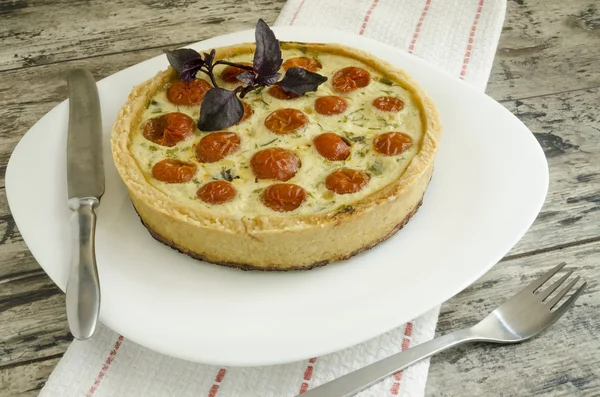 Tart with cherry tomatoes, cheese and onions on white plate, near knife, fork — Stock Photo, Image