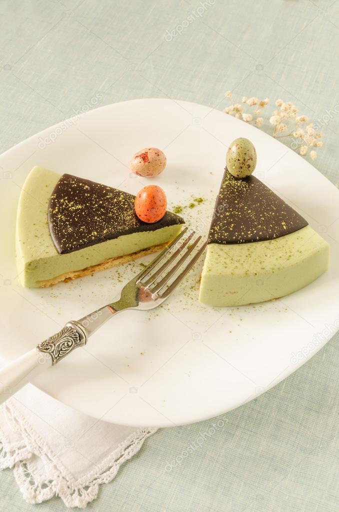 Two pieces of easter cake with tea matcha decorated chocolate ganache and sweet-stuff eggs on white plate