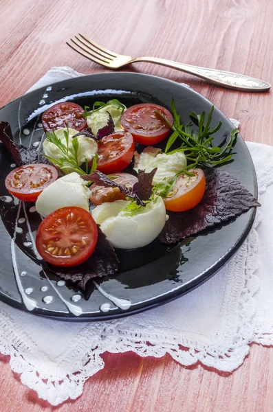 Italské caprese salát s čerstvou bazalkou listy, rajčaty a mozzarellou na červené dřevěný stůl — Stock fotografie