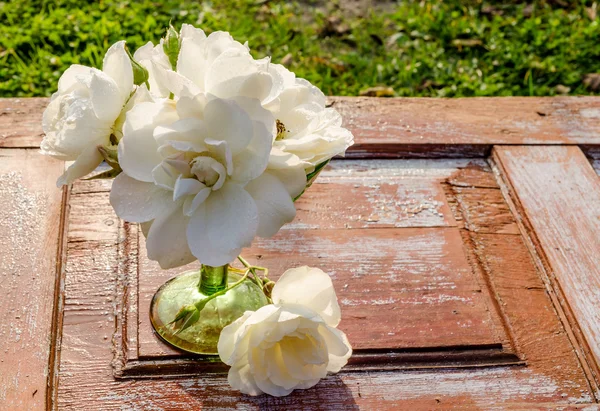 古い木製のテーブルの上に緑色のガラス花瓶の滴とバラの美しい花束 — ストック写真