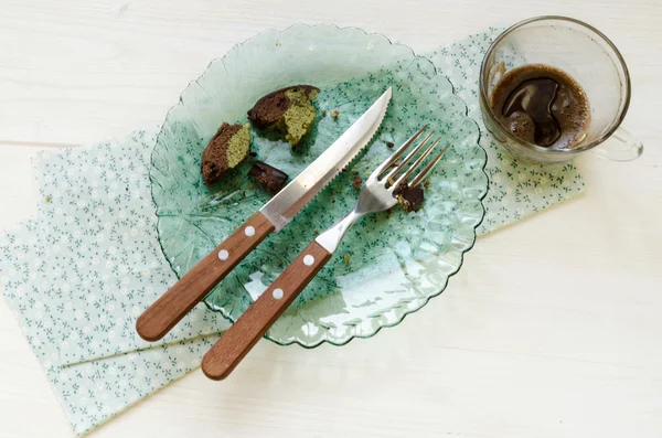 Cuchillo, tenedor y migas de pastel en placa de vidrio. Cerca de taza de café vacía . —  Fotos de Stock