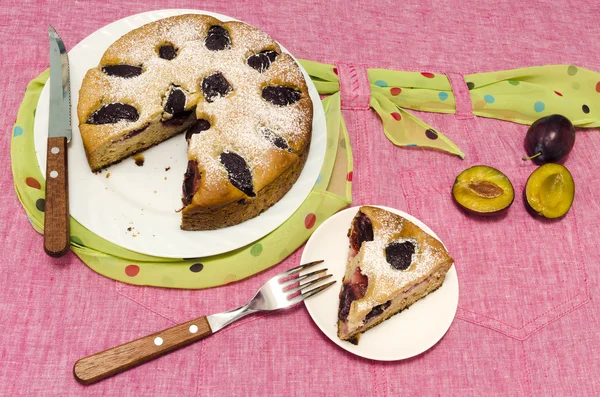 Torta fatta in casa con prugne su una tovaglia rosa. Natura morta . — Foto Stock