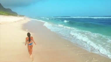 Genç ve çekici bir kadın okyanusun kıyısındaki kumsalda yürürken rahatlıyor. 