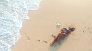 Genç ve çekici bir kadın okyanusun yakınındaki kumsalda dinleniyor.