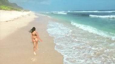 Genç ve çekici bir kadın kumsalda koşuyor ve eğleniyor. 