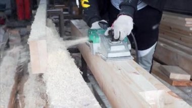 Eldivenli tanımlanamayan marangoz elektrikli uçakla çalışıyor. Bir sürü talaş. Marangoz atölyesi