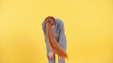 Uzun kızıl saçlı kadın atkuyruğunu komik bir şekilde kıvırıyor. Stüdyoda sarı arka planda.