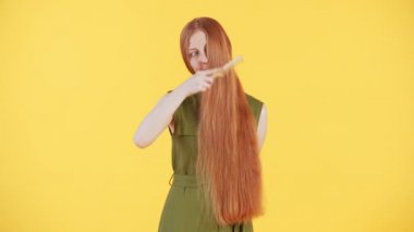 Yüzünde çiller olan genç bir kadın kameraya bakıyor ve uzun yumuşak kızıl saçlarını nazikçe fırçalıyor ve onları okşuyor. Sarı arkaplan