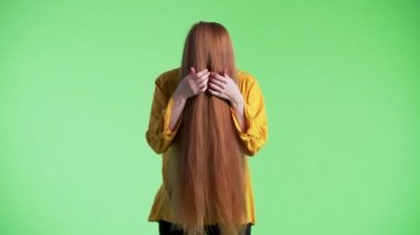 Kadının yüzünde kızıl saçlar var, sonra kameraya bakıp komik suratlar yapıyor. Yeşil arkaplan