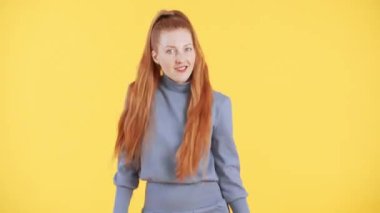 Çilli ve uzun kızıl at kuyruklu kadın kameraya bakıyor ve komik bir şekilde dans ediyor. Sarı arkaplan