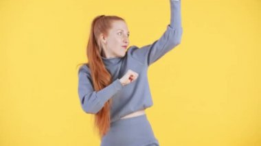 Çilli ve uzun kızıl at kuyruklu kadın kameraya bakıyor ve komik bir şekilde dans ediyor. Sarı arkaplan