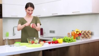 Çekici esmer kadın sebze salatasına tuz ve baharat ekliyor. Genç eş mutfakta akşam yemeği hazırlıyor. Taze sebzeler masada.