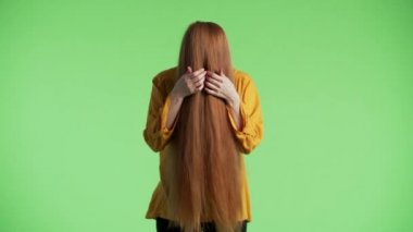 Kadının yüzünde kızıl saçlar var, sonra kameraya bakıp komik suratlar yapıyor. Yeşil arkaplan