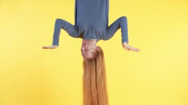 Uzun kızıl saçlı kadın baş aşağı asılı ve sarı arka planda bir şeyi karşılaştırıyor. 