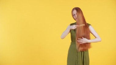 Yüzünde çiller olan genç bir kadın kameraya bakıyor ve uzun yumuşak kızıl saçlarını nazikçe fırçalıyor ve onları okşuyor. Sarı arkaplan