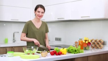 Çekici esmer kadın sebze pişiriyor salata mutfakta salatalık kesiyor. Genç eş mutfakta akşam yemeği hazırlıyor. Taze sebzeler masada.