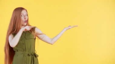 Çilli ve uzun kızıl saçlı güzel bir kadın kameraya bakıyor ve parmakları havada komik bir şekilde dans ediyor. Sarı arkaplan