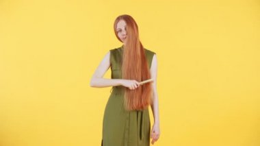 Yüzünde çiller olan genç bir kadın kameraya bakıyor ve uzun yumuşak kızıl saçlarını nazikçe fırçalıyor ve onları okşuyor. Sarı arkaplan