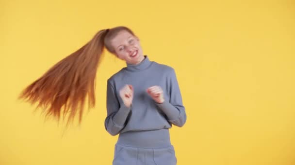 红头发的年轻女子微笑着看着摄像机 跳舞着 黄色背景 — 图库视频影像