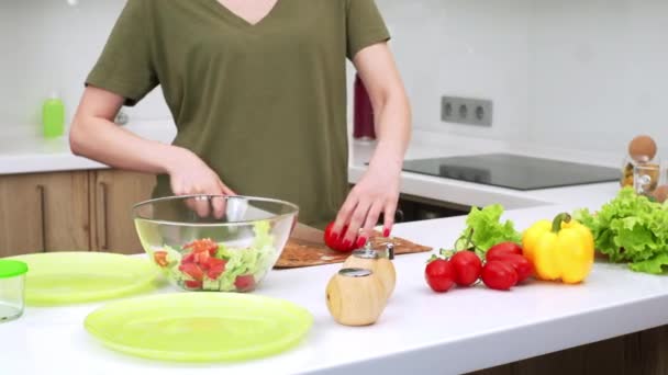 女性がサラダのためにトマトを切っているキッチンテーブルのスライドビュー 若い女性が夕食に野菜サラダを作っています テーブルの上の新鮮な野菜 — ストック動画