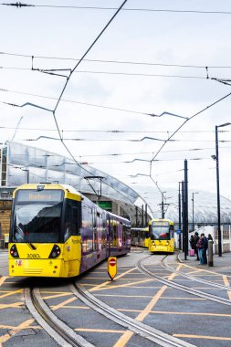 18 Şubat 2026 'da Manchester Victoria İstasyonu' nun modern mimari tepe örtüsünün dışındaki raylarda gezinen iki sarı Metrolink tramvayı.