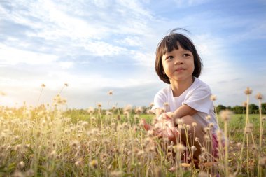 Taylandlı bir kız çocuğu, 4-6 yaşlarında, sevimli bir yüzü var, açık havada oynuyor. Yüzünde mutlu bir gülümseme vardı. Arka plan yeşil alanlar ve mavi gökyüzü. Tatilde olmak güzel bir şey..
