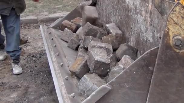 Les travailleurs chargent des pierres de granit de la surface de la route dans le godet de la pelle — Video