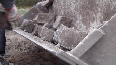 İşçiler yol yüzeyinden kazıcı kovasına granit taşlar yüklüyorlar.