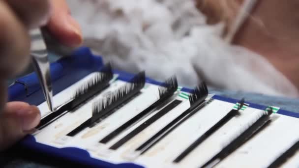 The master takes the eyelashes from the package for gluing to the patient with tweezers — Stock Video