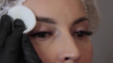 Güzellik salonunda, usta, modelin kaşlarındaki makyajı, yuvarlak beyaz pamuklu çubukla temizler. Kafkasyalı güzel bir modelin yüzüne yakın çekim. Yüz bakımı kavramı