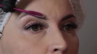 Güzellik salonunda, usta modelin kaşlarına boya yapmadan önce fırçayla temizlemek için şampuan sürer. Kafkasyalı güzel bir modelin yüzüne yakın çekim. Cilt bakımı kavramı