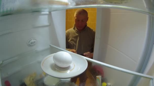 若い男が冷蔵庫のドアを開けて中を見る 冷蔵庫に卵が一つある これ以上の製品は 彼は手で卵に触れ 失望し 冷蔵庫のドアを閉じます キッチン冷蔵庫からの眺め — ストック動画