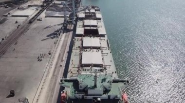 Bir limanda tahıl yükleyen büyük bir geminin üzerinde konveyör makinesiyle kamera uçuşu. Buğday ihracatı. Deniz ihracatı. Tarım. Kuş bakışı. hava görüntüsü