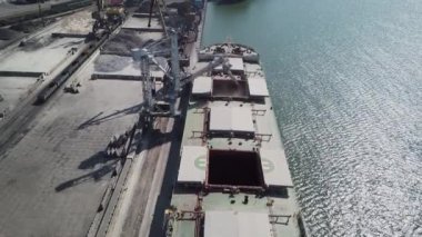 Bir limanda tahıl yükleyen büyük bir geminin üzerinde konveyör makinesiyle kamera uçuşu. Buğday ihracatı. Deniz ihracatı. Tarım. Kuş bakışı. hava görüntüsü