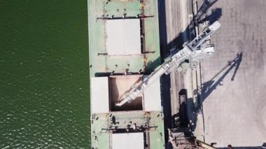 Denizden buğday nakli için limana demirlemiş bir tüccar gemisini yüklemek için taşıyıcı tipi bir yükleme makinesi. Buğday ihracatı. Deniz ihracatı. Tarım. Kuş bakışı. hava görüntüsü