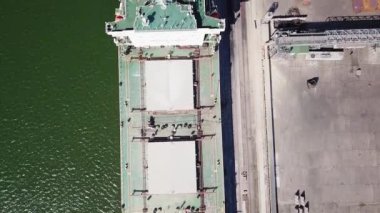 Kameranın büyük bir deniz gemisinin üzerinden geçişi. Kamera aşağıya bakıyor. Gemi limana demirlemiş, tahıl yükleme makinesiyle. Buğday ihracatı. Deniz ihracatı. hava görüntüsü