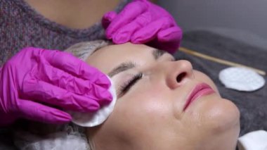 Güzellik salonunda kadın kaşlarının düzeltilmesi için prosedürler. Müşterinin yüzüne ve stilistin ellerine yakın çekim. Usta, işlemden önce modelin kaşlarını pamukla siler.