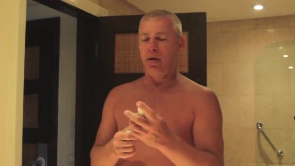 Een man voor de spiegel in de badkamer besprenkelt zijn gezicht met aftershave — Stockvideo