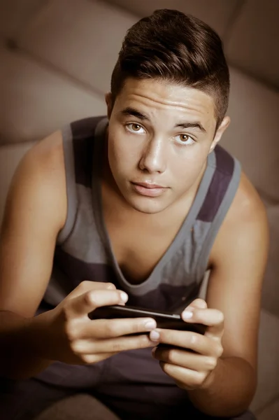 Adolescente jugando juegos en línea con el teléfono inteligente sentado en el sofá —  Fotos de Stock