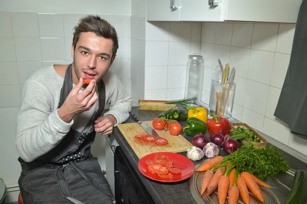 Uomo che taglia e mangia verdure in cucina — Foto Stock