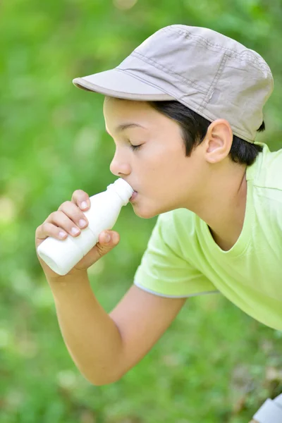 TeYoung boy sitting in the grass drinking milk drink — Stock Photo, Image