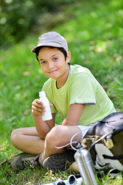 Мальчик, сидящий в траве и пьющий молочный напиток — стоковое фото