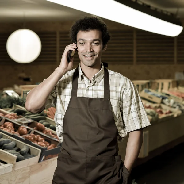 Grocery clerk phoning in produce aisle of supermarket store — Stock Photo, Image