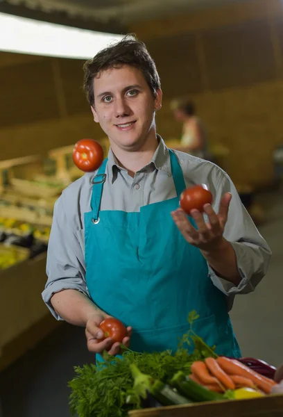 Escriturário de mercearia malabarismo com tomates em loja de supermercado — Fotografia de Stock