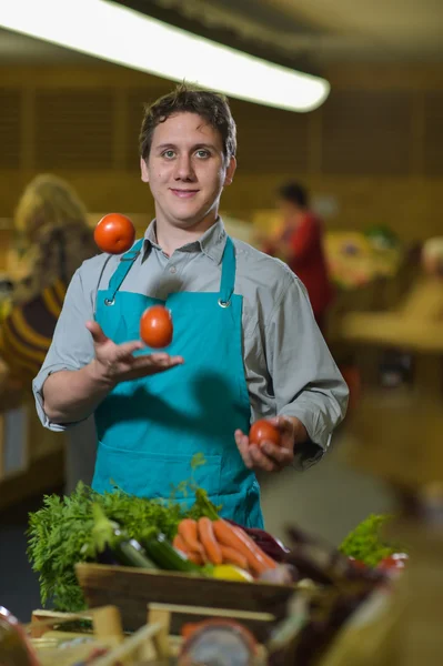 Escriturário de mercearia malabarismo com tomates em loja de supermercado — Fotografia de Stock