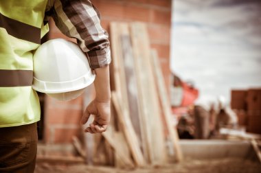 Bir kask inşaat sitenin arka planı ile holding işçi.