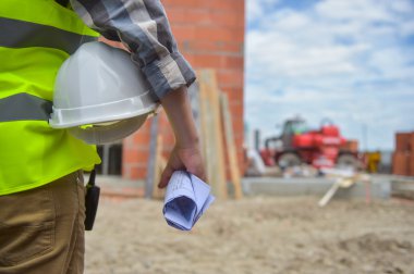 Bir kask inşaat sitenin arka planı ile holding işçi.