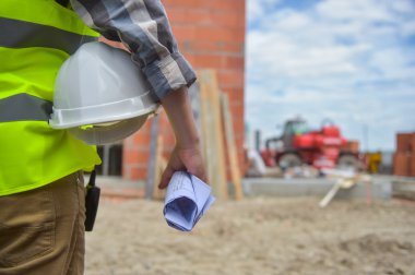 Worker holding a helmet with background of construction site. clipart