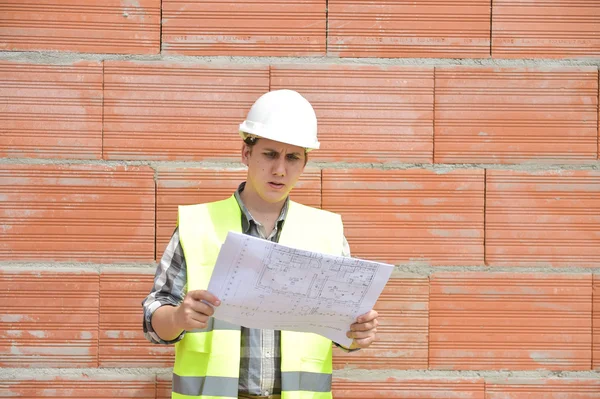 Інженер будівельник перед оранжевою цегляною стіною з планом — стокове фото